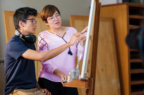 man with headset helping woman paint on canvas